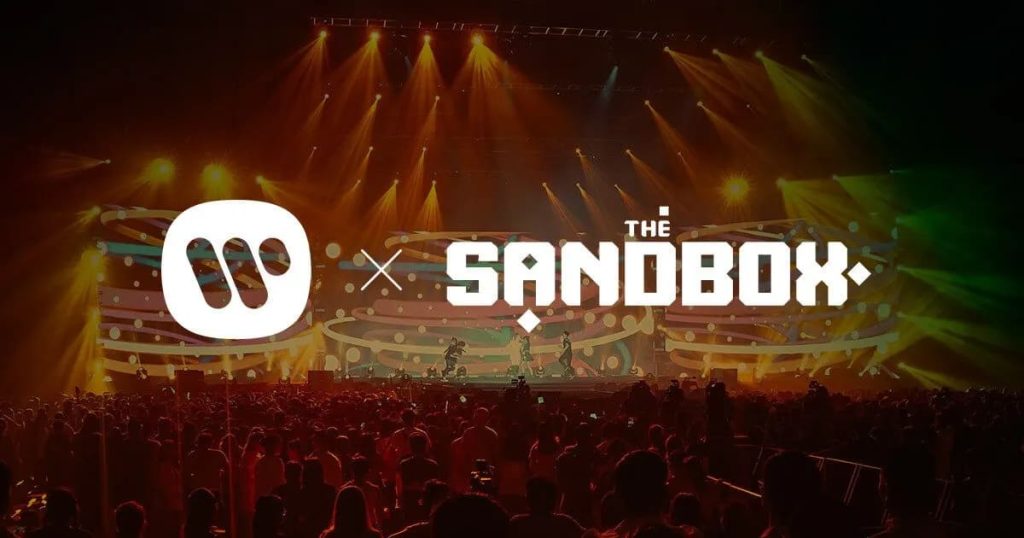 Sandbox Metaverse Unveils AR Music Experience With Warner picture of the Sandbox metaverse logo and Warner Music logos side by side superimposed over a convert crowd